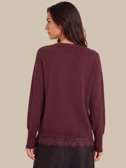 A woman shown from the back wearing a long-sleeve crewneck sweater in a deep burgundy or plum color, featuring a lace hem detail, against a solid beige background.