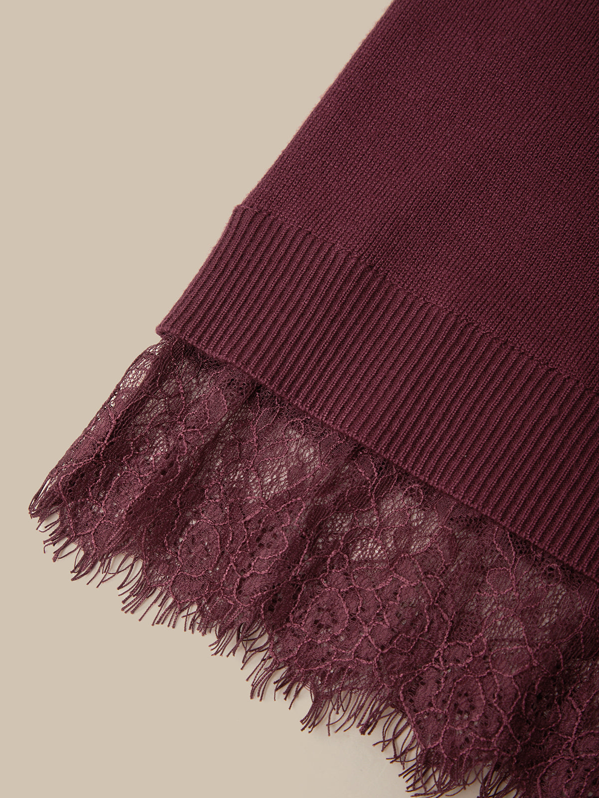 Close-up of a burgundy knit fabric with a wide ribbed cuff and a matching lace trim with frayed edges, shown on a light beige background.