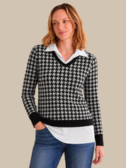 Woman wearing a black and white houndstooth patterned sweater over a white shirt with blue jeans on a beige background