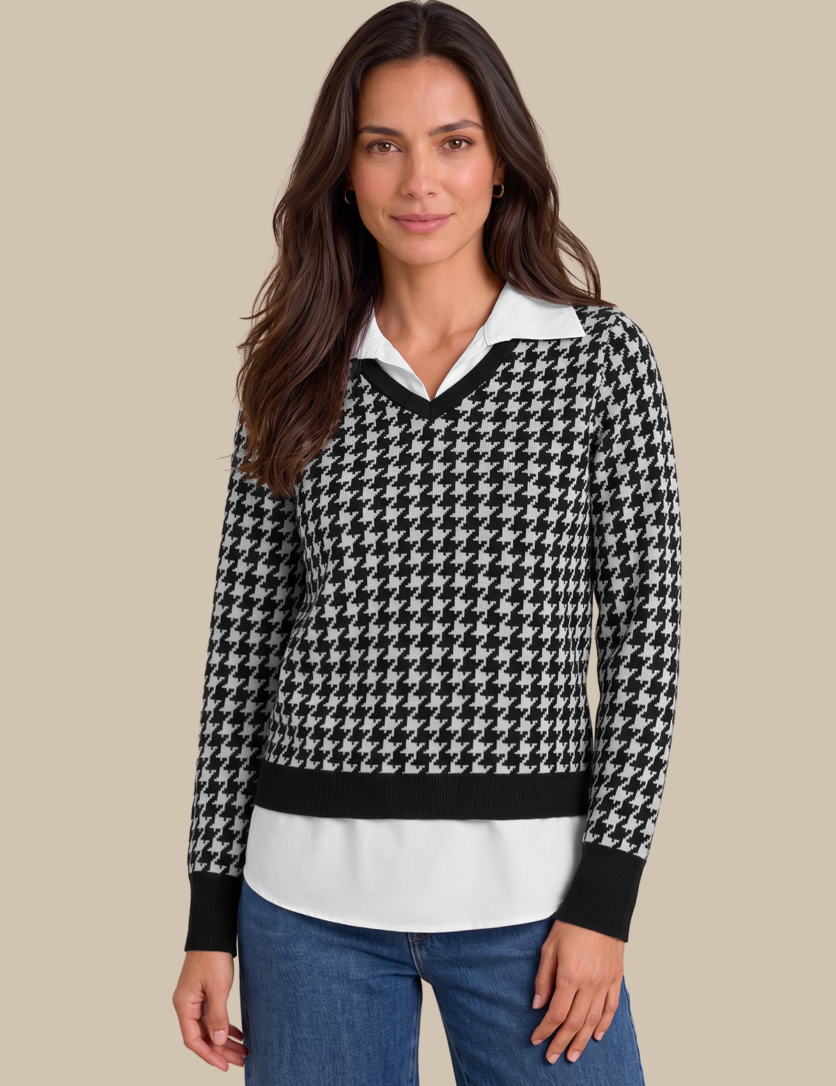 A woman modeling a black and white houndstooth knit sweater with a white collar and black trim, paired with blue jeans, against a solid beige background.