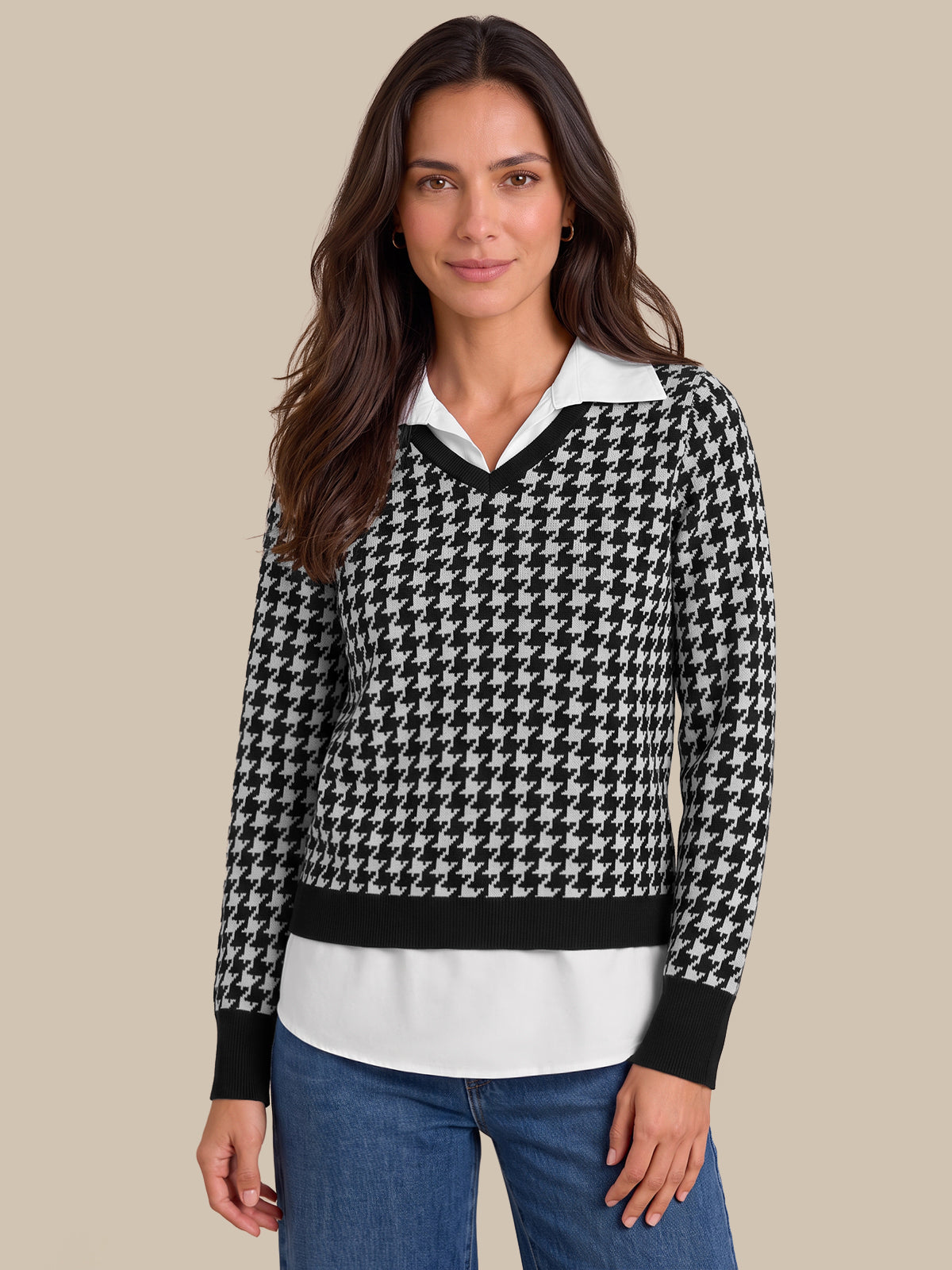 A woman modeling a black and white houndstooth knit sweater with a white collar and black trim, paired with blue jeans, against a solid beige background.