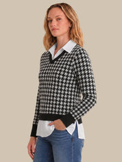 Woman wearing a houndstooth pattern sweater over a white shirt with blue jeans on a beige background