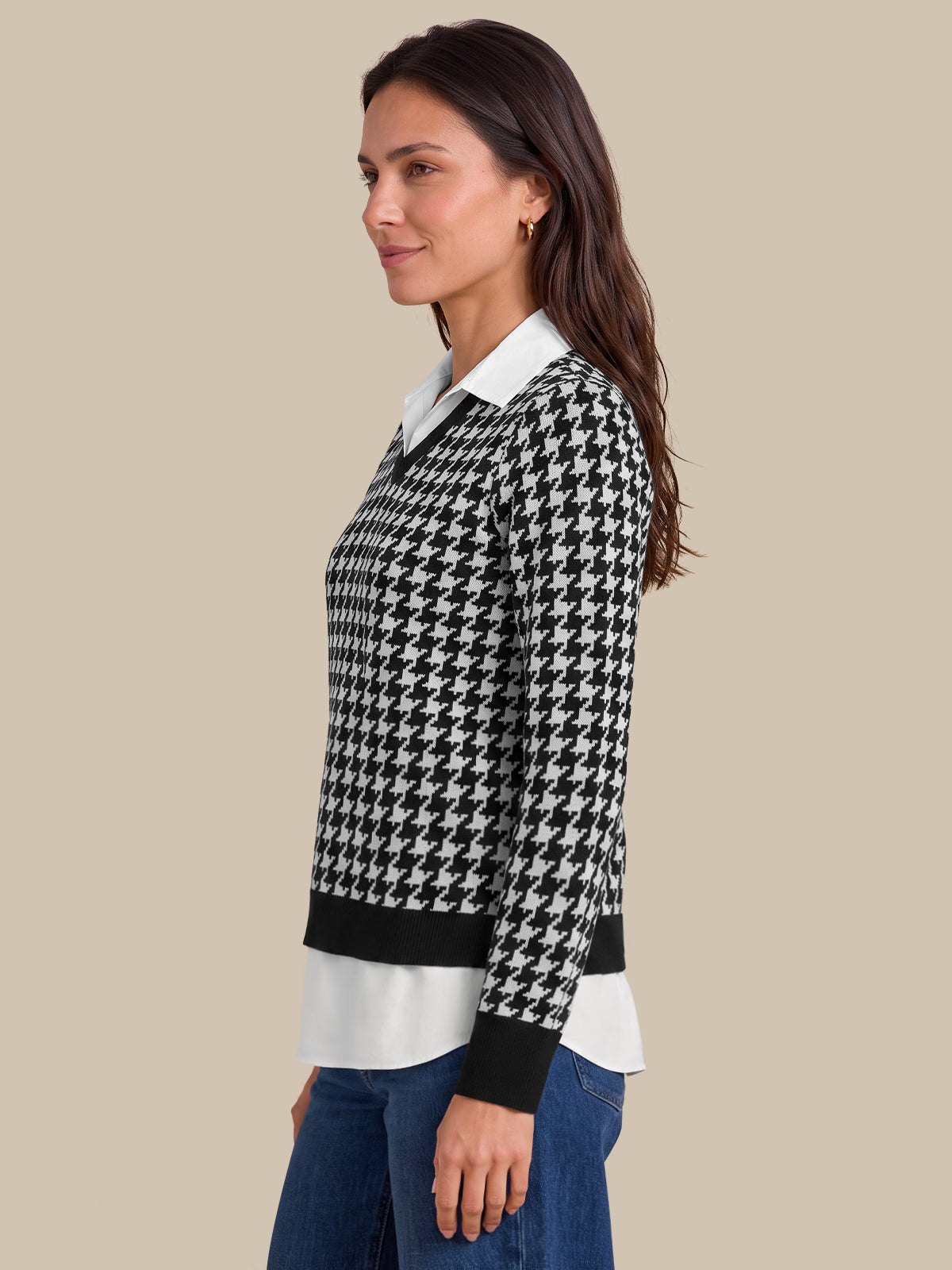 A woman shown in side profile wearing a black and white houndstooth knit sweater over a white collared shirt and blue jeans, against a solid beige studio background.
