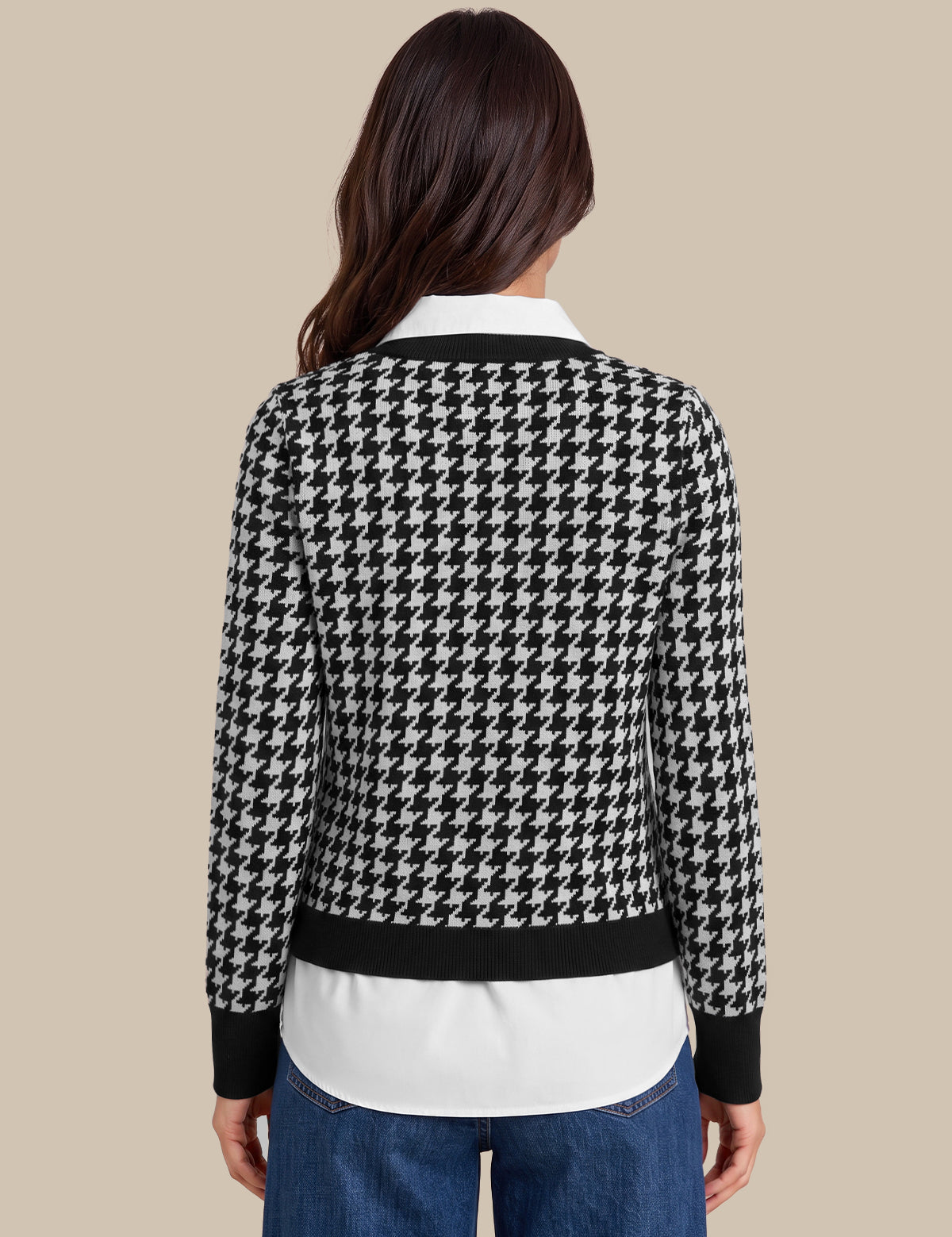 A woman viewed from the back wearing a black and white houndstooth cardigan over a white collared shirt and blue jeans, set against a solid beige background.
