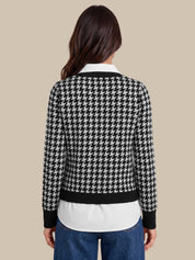 A woman viewed from the back wearing a black and white houndstooth cardigan over a white collared shirt and blue jeans, set against a solid beige background.