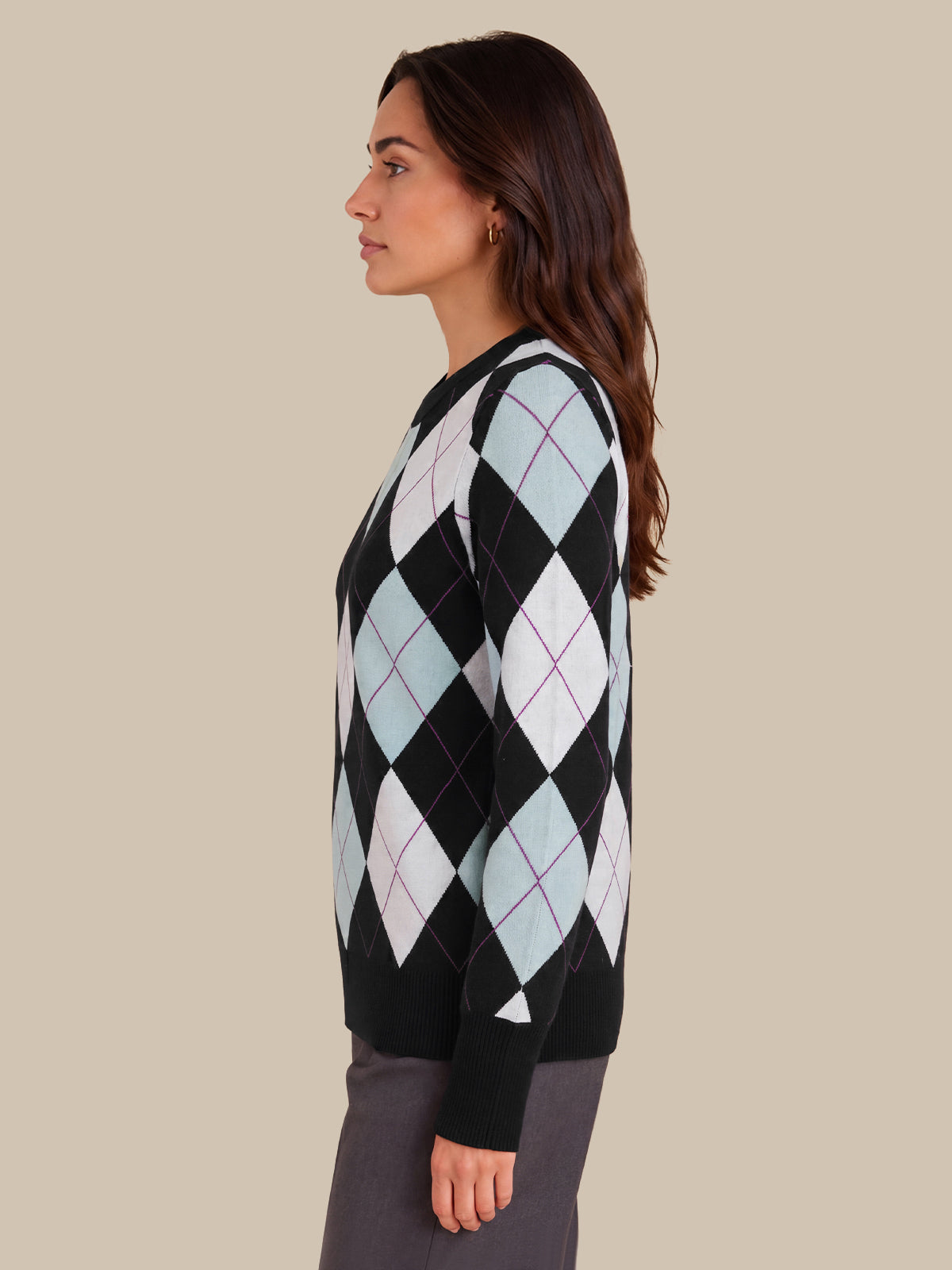 A woman shown in side profile wearing a black knit sweater with a light blue, white, and purple argyle pattern, paired with dark gray trousers, against a solid beige background.