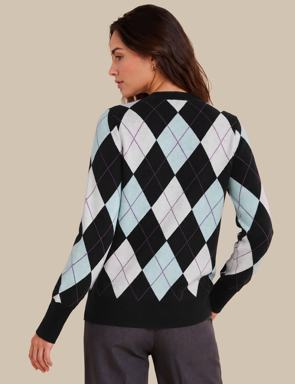 A woman shown from the back wearing a black sweater with a light blue, white, and black argyle pattern, paired with dark gray trousers, against a solid beige background.