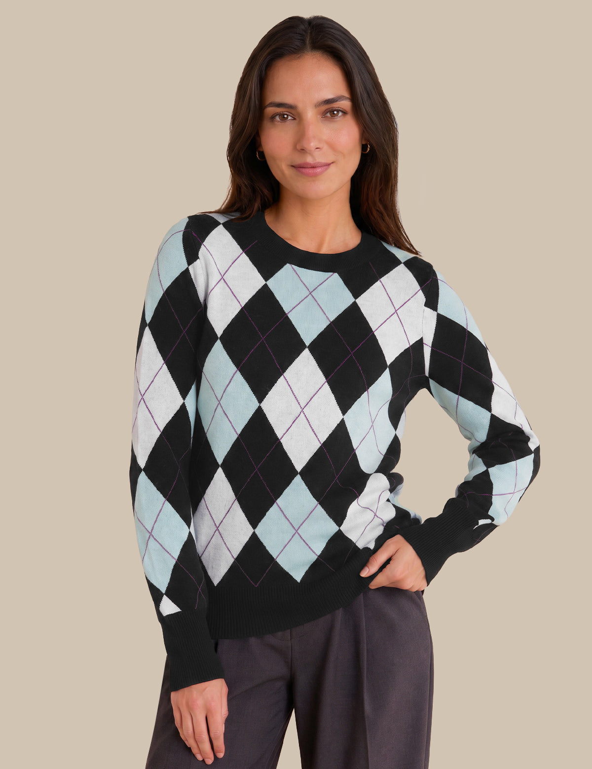 A woman modeling a black long-sleeve sweater with a light blue and white argyle pattern, paired with dark gray trousers, against a solid beige background.
