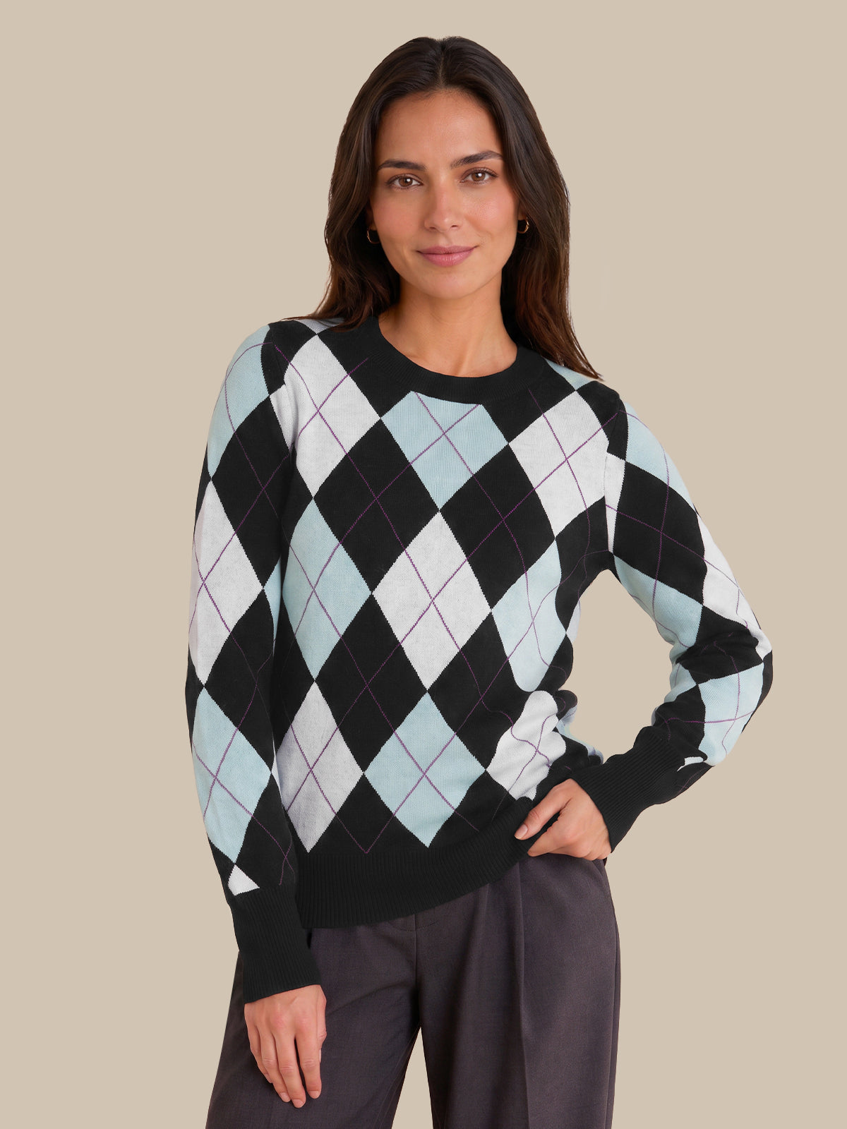 A woman modeling a black long-sleeve sweater with a light blue and white argyle pattern, paired with dark gray trousers, against a solid beige background.