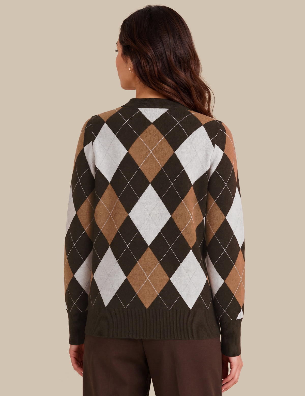 A woman viewed from the back wearing a long-sleeve knit sweater with an argyle pattern in dark brown, tan, and white, paired with dark brown pants, against a solid beige background.