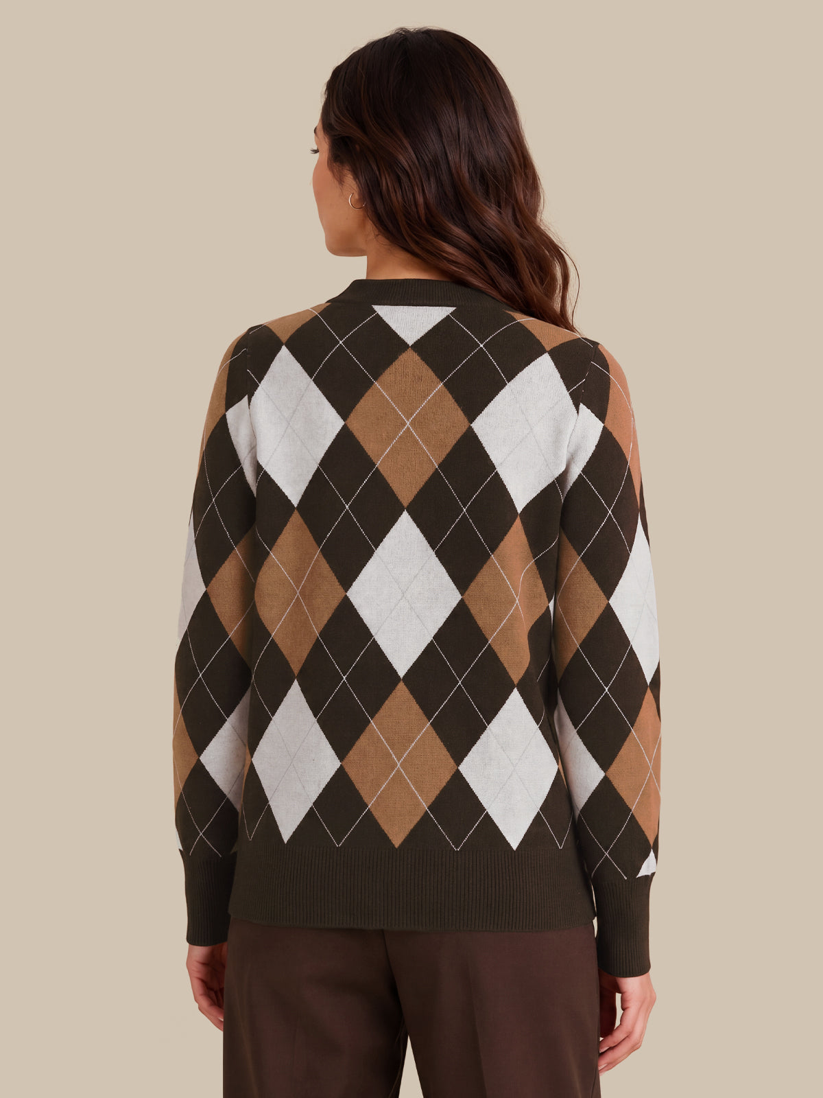 A woman viewed from the back wearing a long-sleeve knit sweater with an argyle pattern in dark brown, tan, and white, paired with dark brown pants, against a solid beige background.