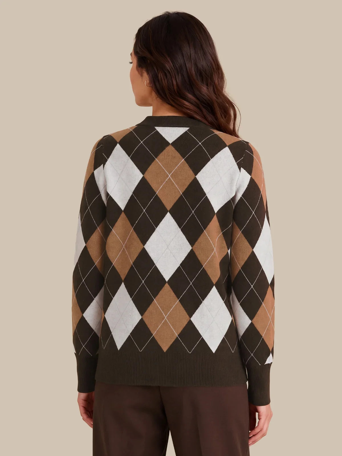 A woman viewed from the back wearing a long-sleeve argyle sweater with dark brown, tan, white, and black diamonds, paired with dark brown pants, against a solid beige background.