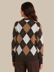 A woman viewed from the back wearing a long-sleeve argyle sweater with dark brown, tan, white, and black diamonds, paired with dark brown pants, against a solid beige background.