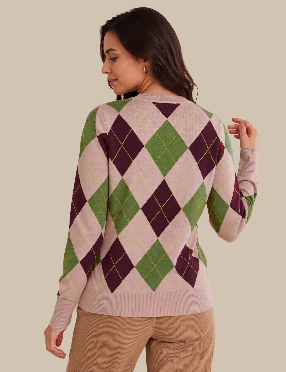 A woman shown from the back wearing a long-sleeve knit sweater with an argyle pattern in light pink, green, and dark purple, paired with tan pants, against a solid beige background.