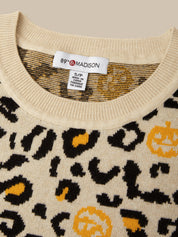 Close-up of a cream knit sweater with a black leopard print and yellow pumpkin motifs. The inside collar shows a white tag reading 89th Madison.