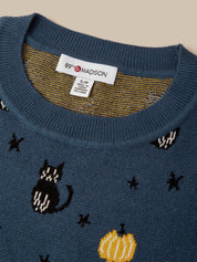 Close-up of a blue knit sweater with a crew neck, featuring a white 89th & Madison brand label inside the collar. The sweater has a pattern of black cats, yellow pumpkins, and black stars on a beige background.