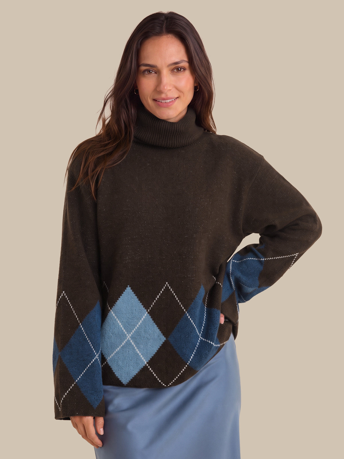 A woman wearing a dark brown turtleneck sweater with an argyle pattern in blue and brown on the lower half, paired with a light blue skirt, against a solid beige background.