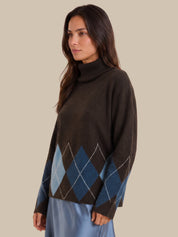 A woman wearing a dark brown turtleneck sweater with a blue and gray argyle pattern on the lower front and sleeves, paired with a light blue skirt, set against a solid beige background.