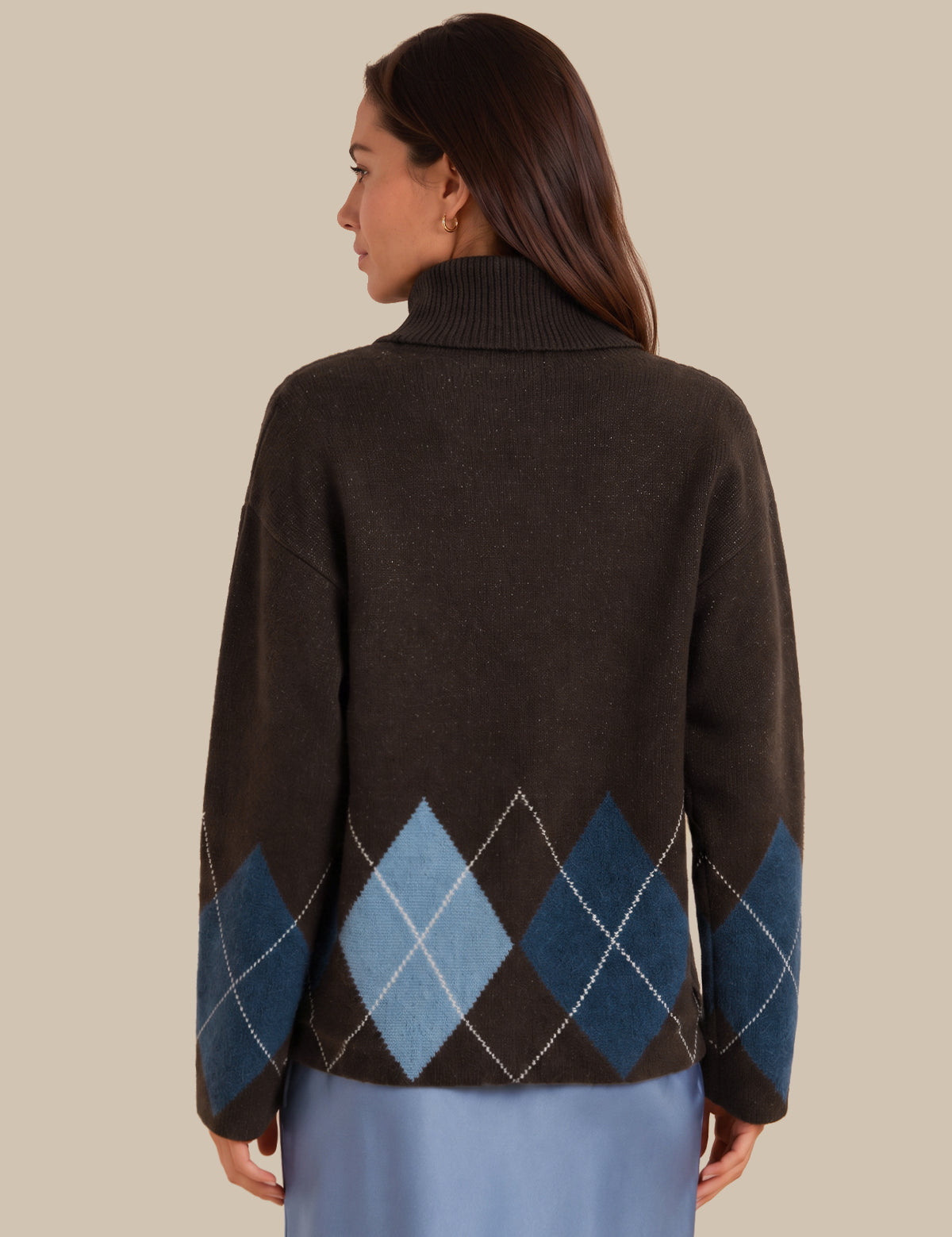 A woman shown from the back wearing a dark brown knit sweater with an argyle pattern in shades of blue and light gray, paired with a light blue skirt, against a solid beige background.