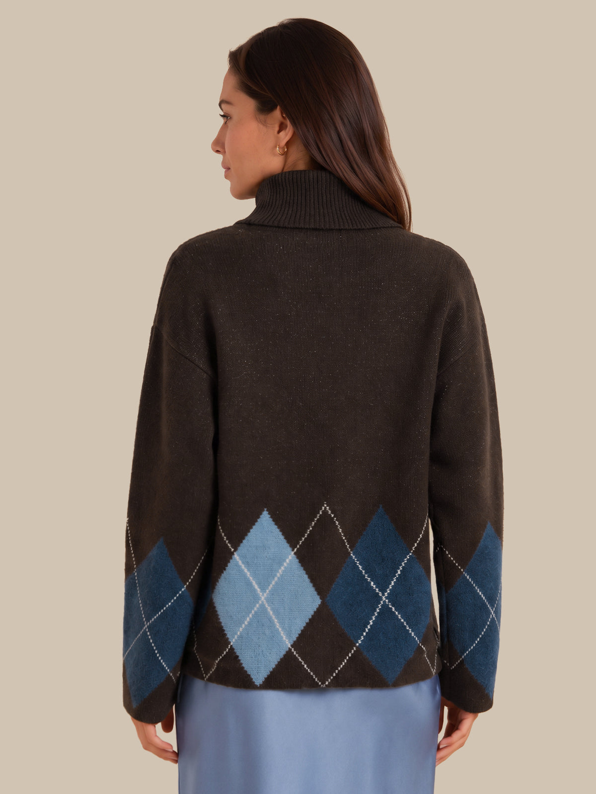 A woman shown from the back wearing a dark brown knit sweater with an argyle pattern in shades of blue and light gray, paired with a light blue skirt, against a solid beige background.