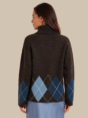 A woman shown from the back wearing a dark brown knit sweater with an argyle pattern in shades of blue and light gray, paired with a light blue skirt, against a solid beige background.