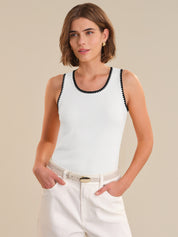 Woman wearing a white tank top with black trim against a beige background