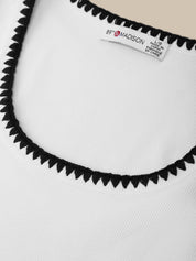 Close-up of a white garment with black trim and a visible label on a light gray background.