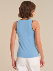 Woman wearing a light blue sleeveless top with white pants on a beige background