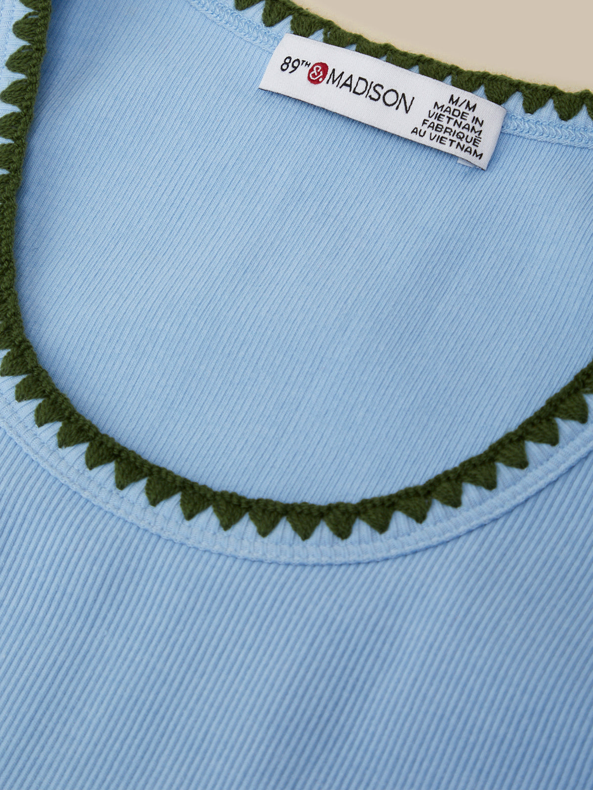 Close-up of a blue garment with green trim and a label on a beige background
