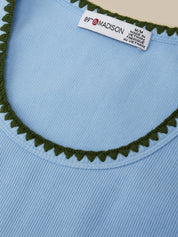 Close-up of a blue garment with green trim and a label on a beige background