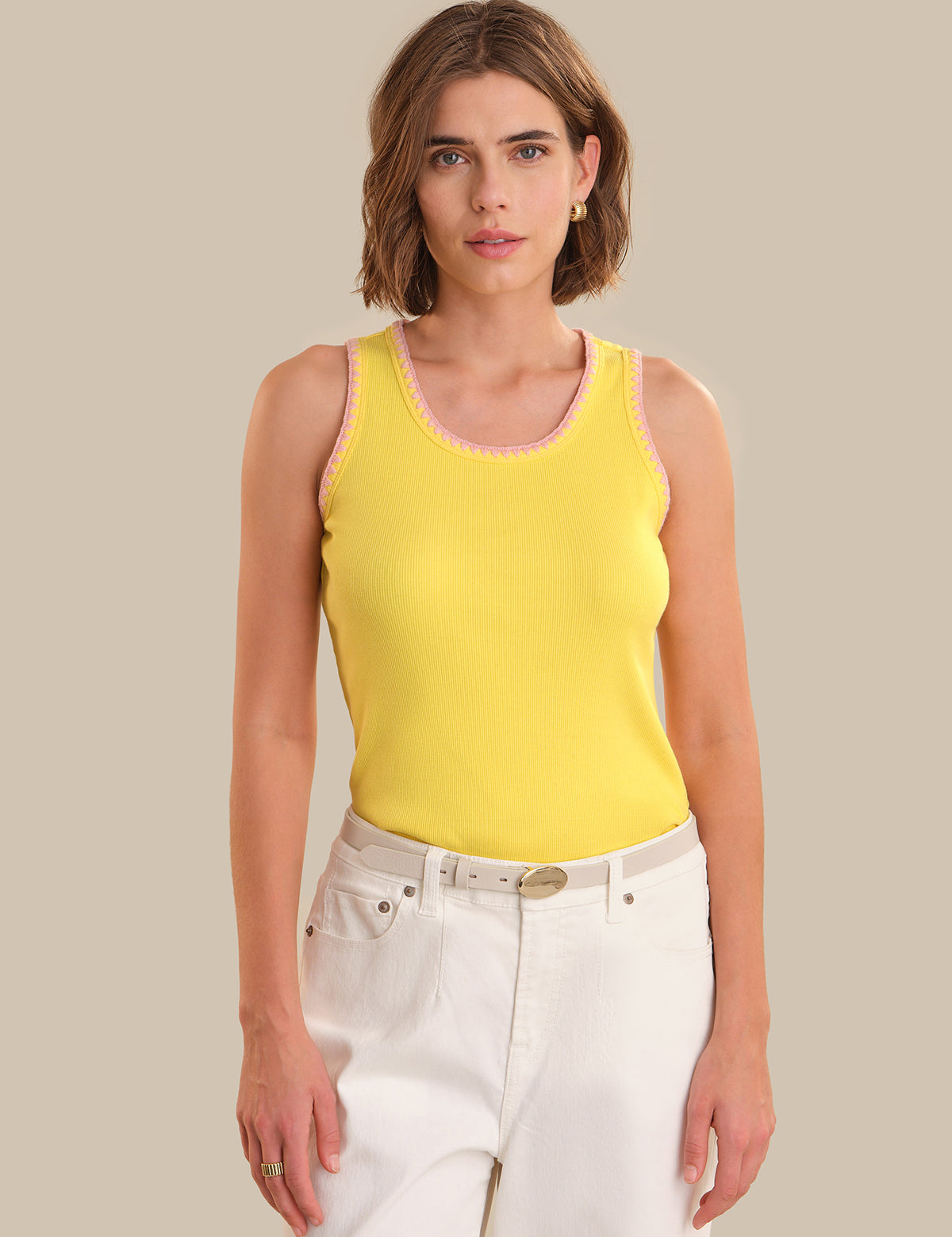 Woman wearing a yellow tank top and white pants against a beige background