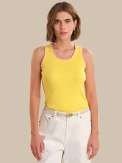Woman wearing a yellow tank top and white pants against a beige background