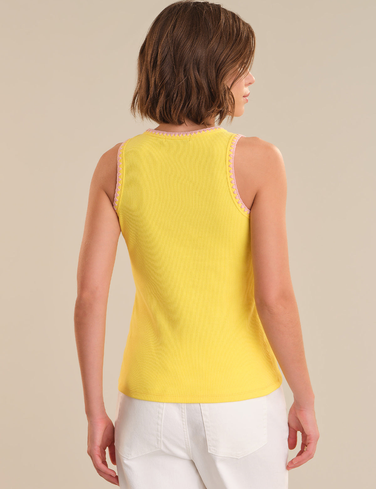 Woman wearing a yellow sleeveless top and white pants against a beige background