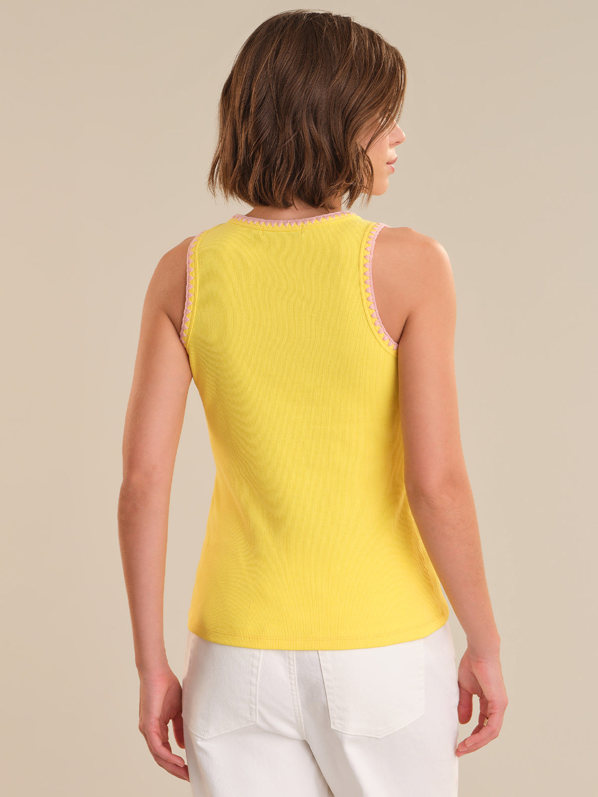 Woman wearing a yellow sleeveless top and white pants against a beige background