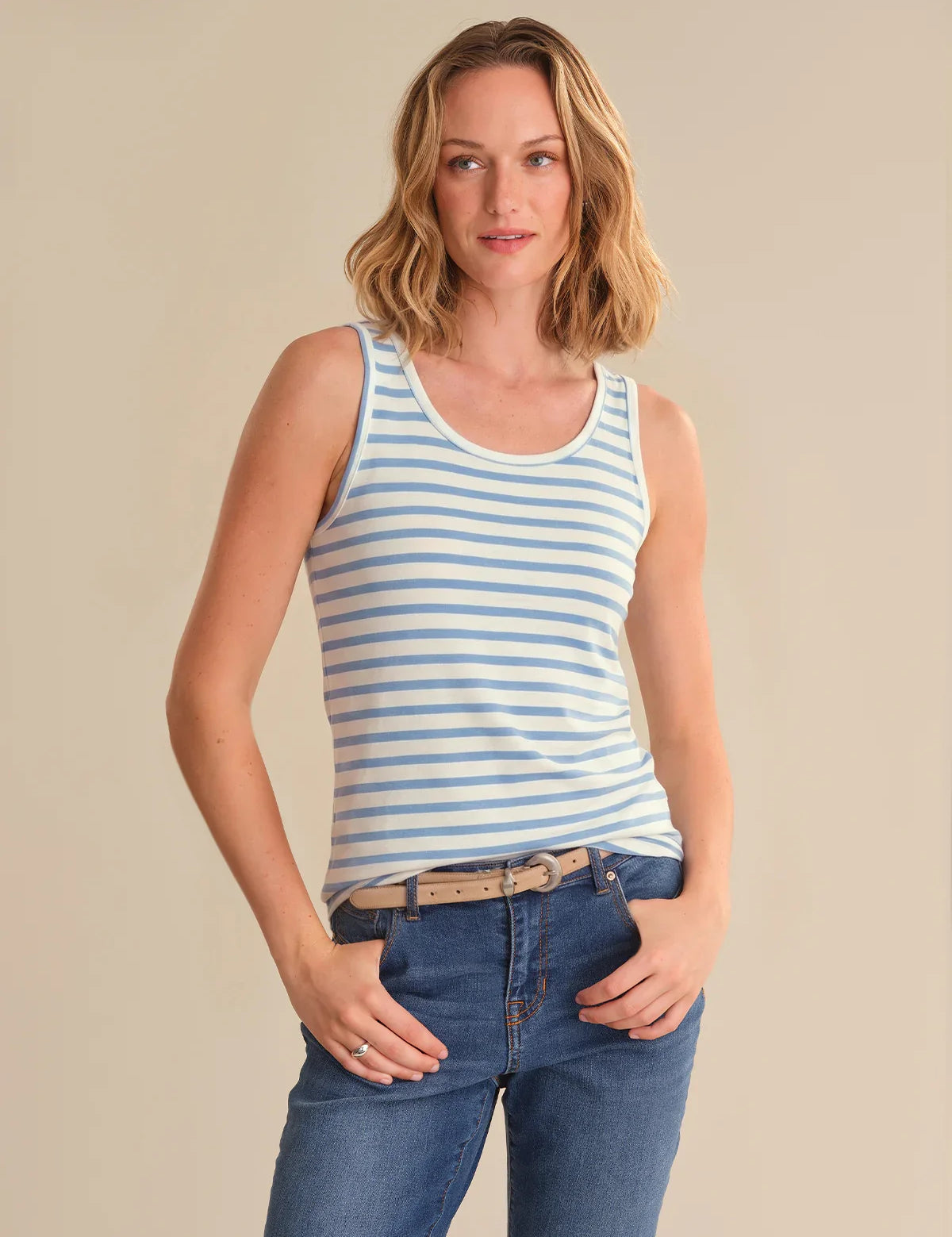 Woman wearing a striped tank top and jeans against a beige background