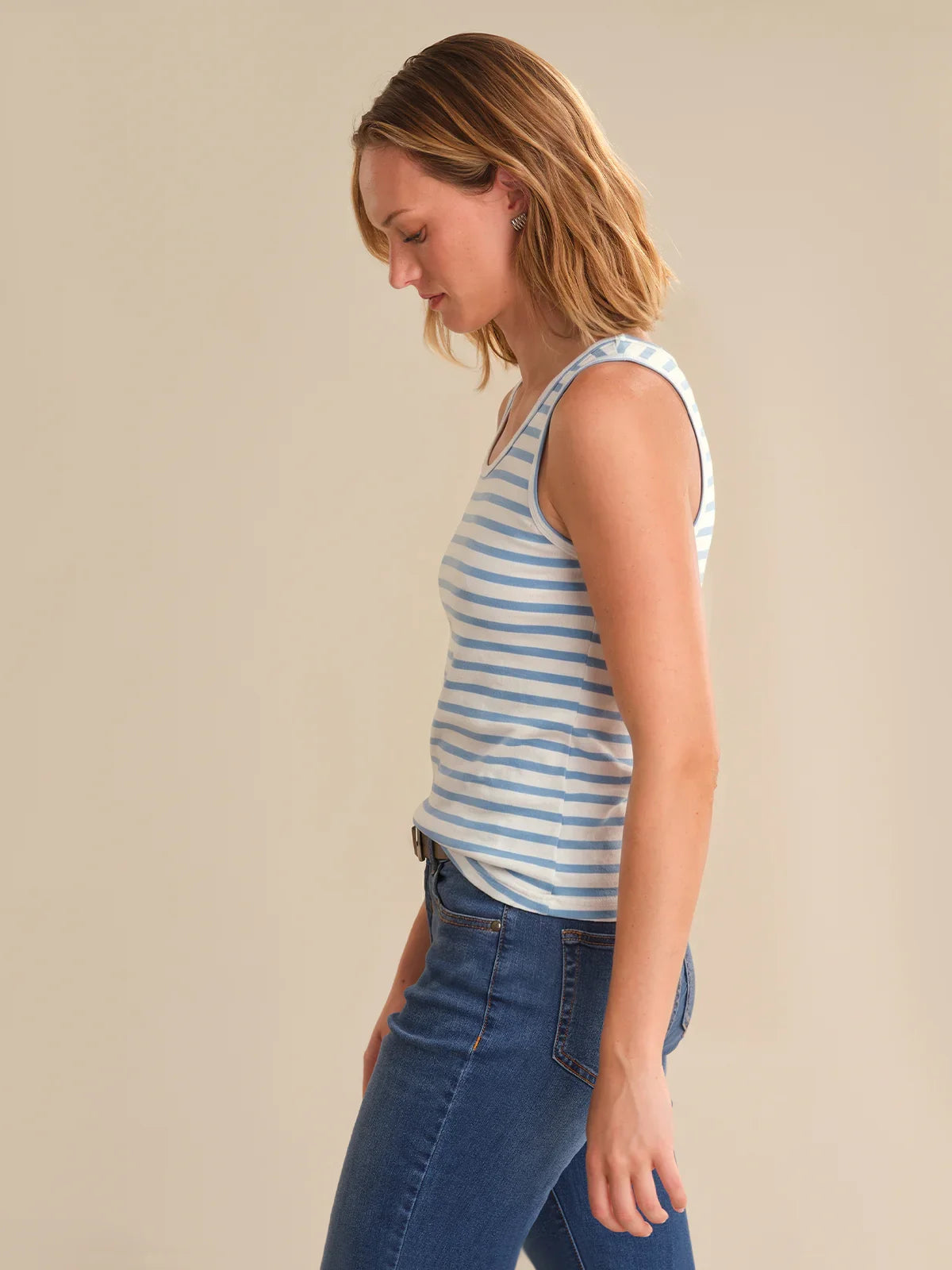 Woman wearing a striped tank top and blue jeans against a beige background