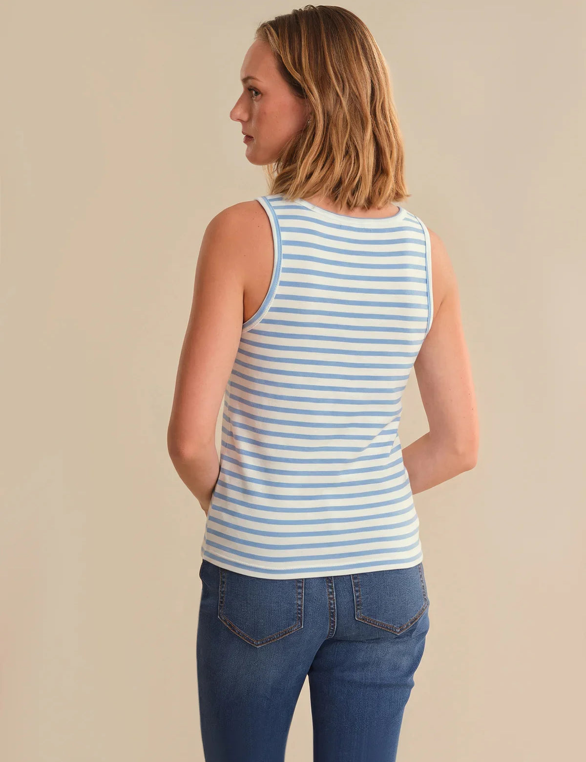 Woman wearing a blue and white striped tank top and blue jeans on a beige background