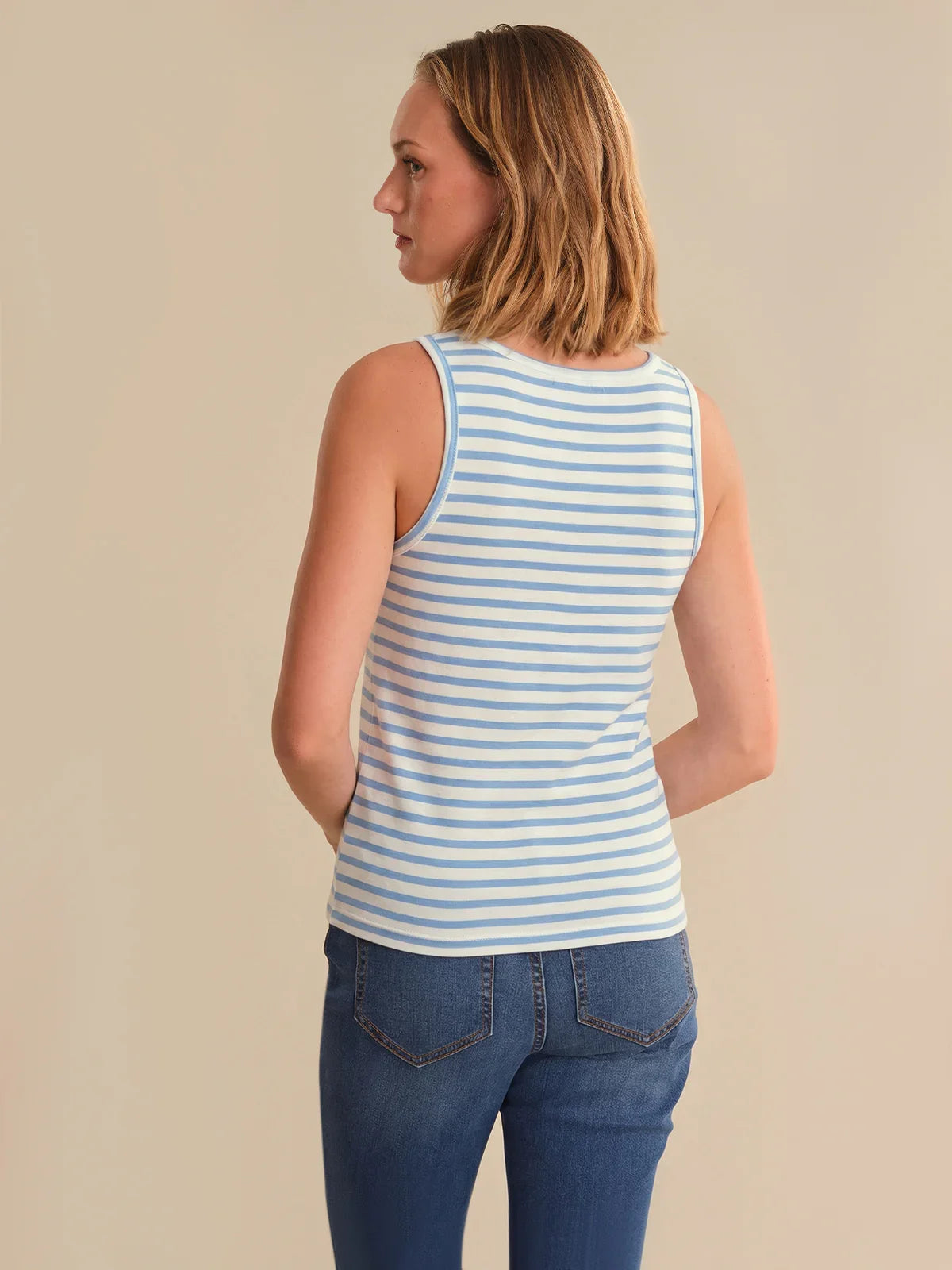 Woman wearing a blue and white striped tank top and blue jeans on a beige background