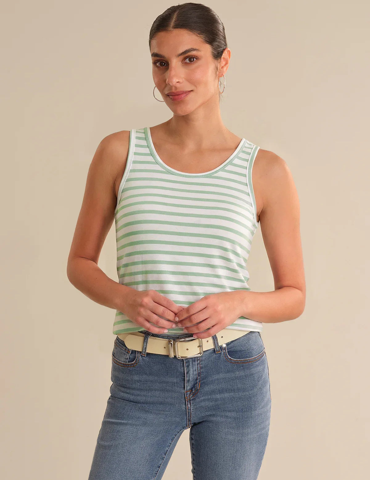 Woman wearing a green and white striped tank top and blue jeans on a beige background