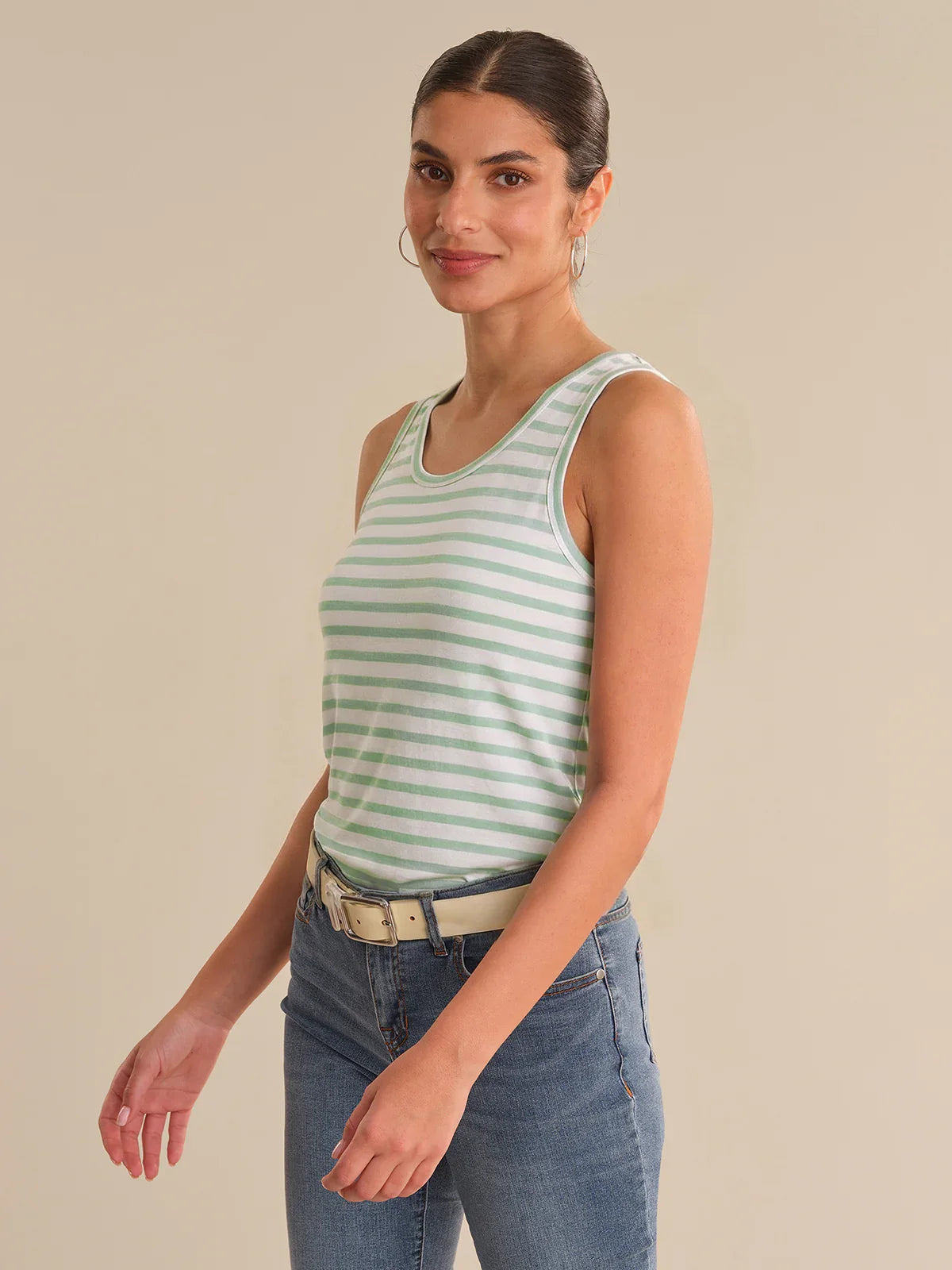 Woman wearing a green and white striped tank top and blue jeans on a beige background