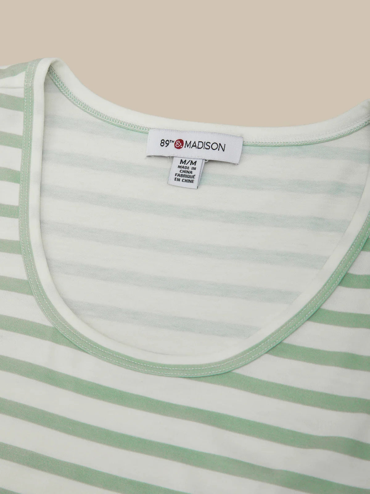 Close-up of a green and white striped shirt with a brand label on a beige background