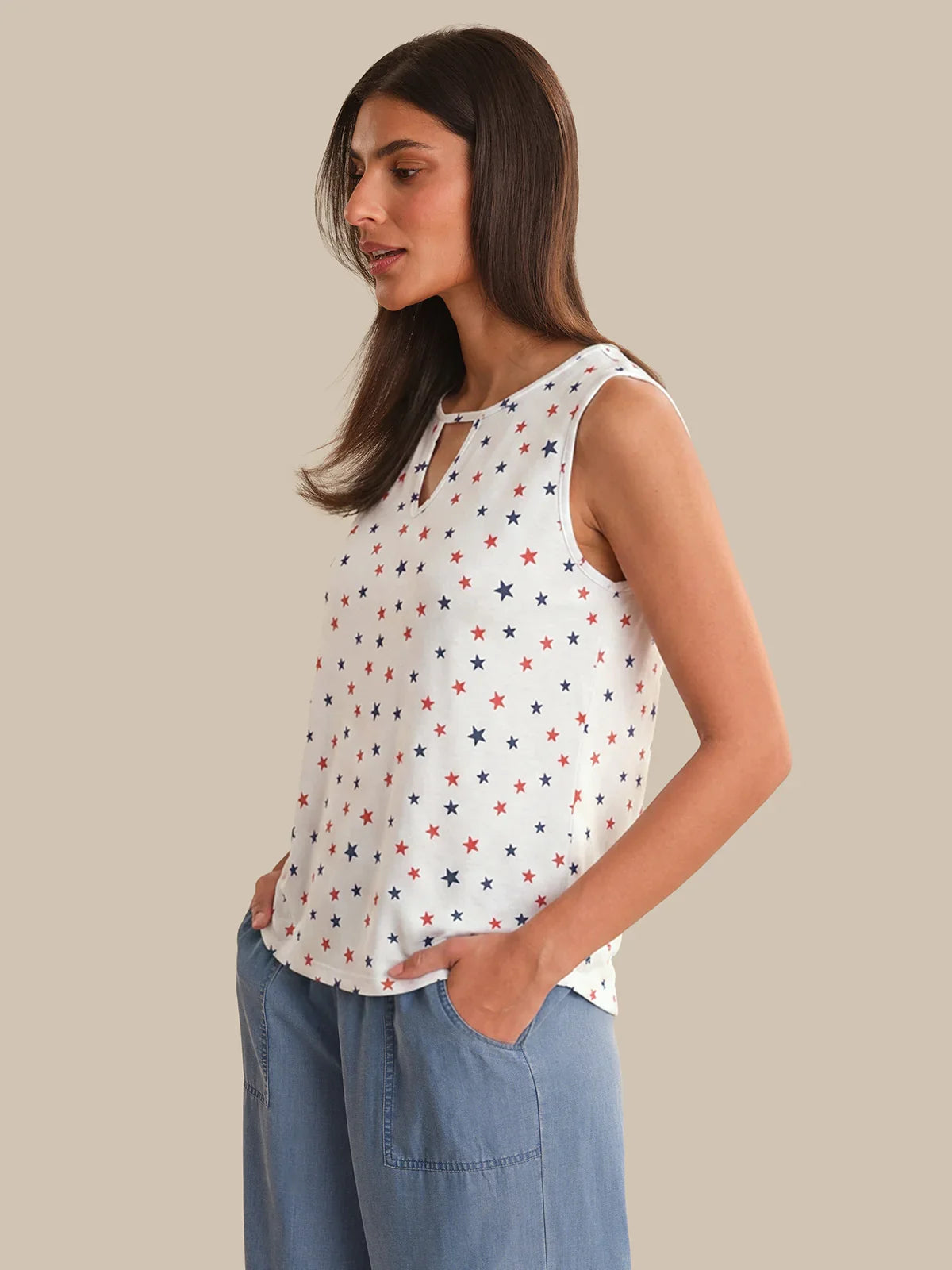 Woman wearing a sleeveless top with star pattern and blue pants on a beige background