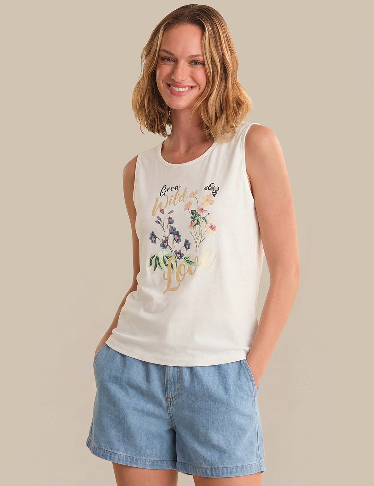Woman wearing a white sleeveless top with floral designs and blue shorts on a beige background