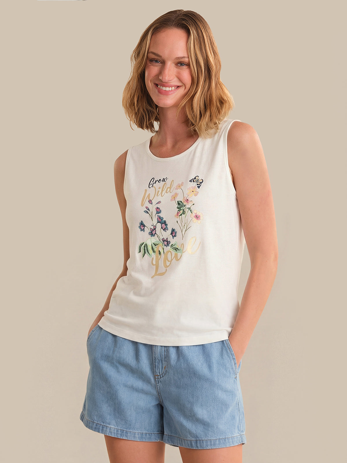 Woman wearing a white sleeveless top with floral designs and blue shorts on a beige background