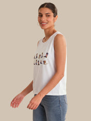 Woman wearing a white sleeveless shirt with text and blue jeans on a beige background