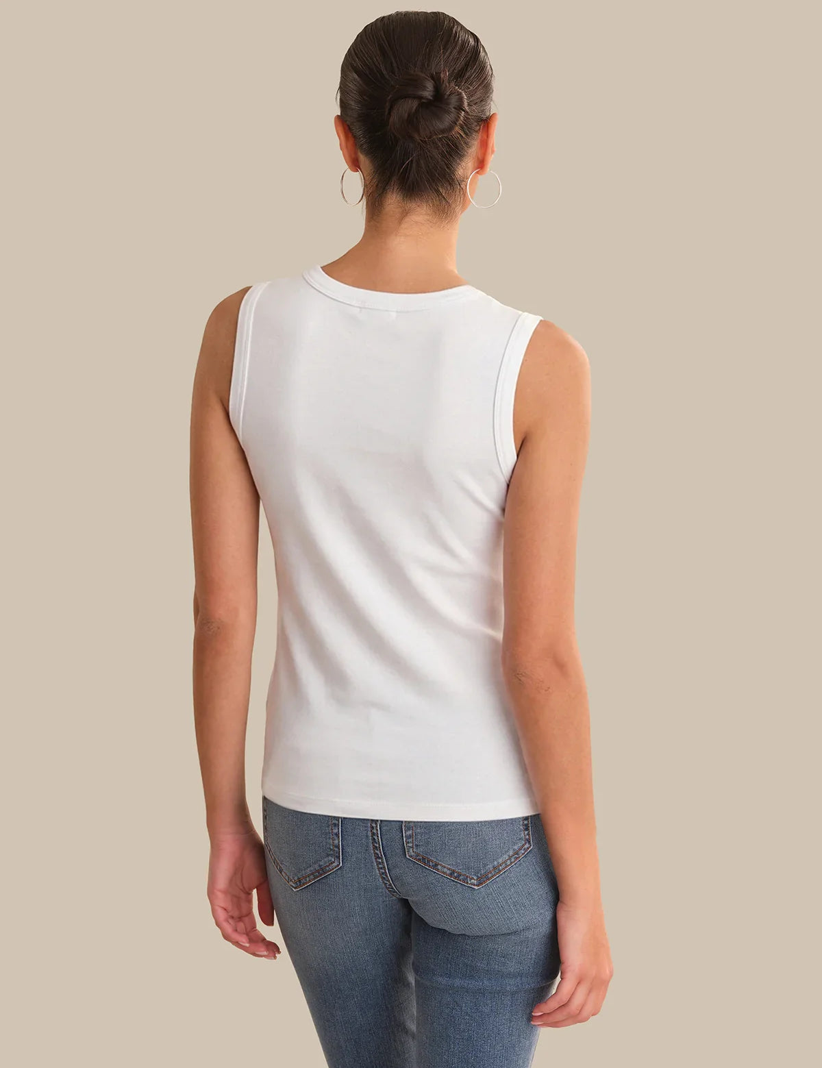 Person wearing a white sleeveless top and blue jeans on a beige background