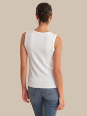 Person wearing a white sleeveless top and blue jeans on a beige background