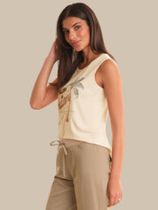 Woman wearing a beige sleeveless top with graphic design and beige pants against a plain background