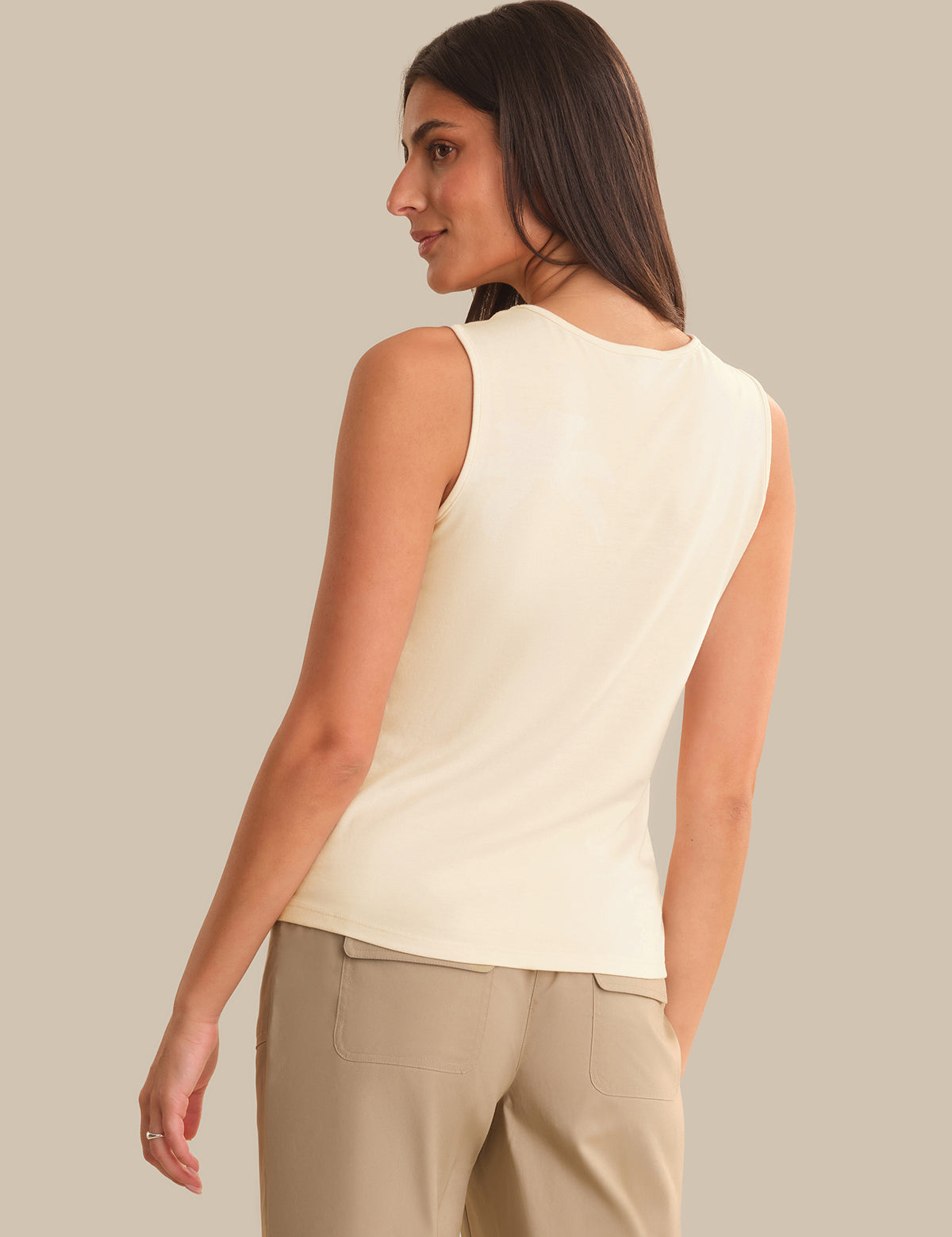 Woman wearing a light-colored sleeveless top and beige pants against a neutral background