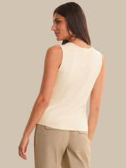Woman wearing a light-colored sleeveless top and beige pants against a neutral background